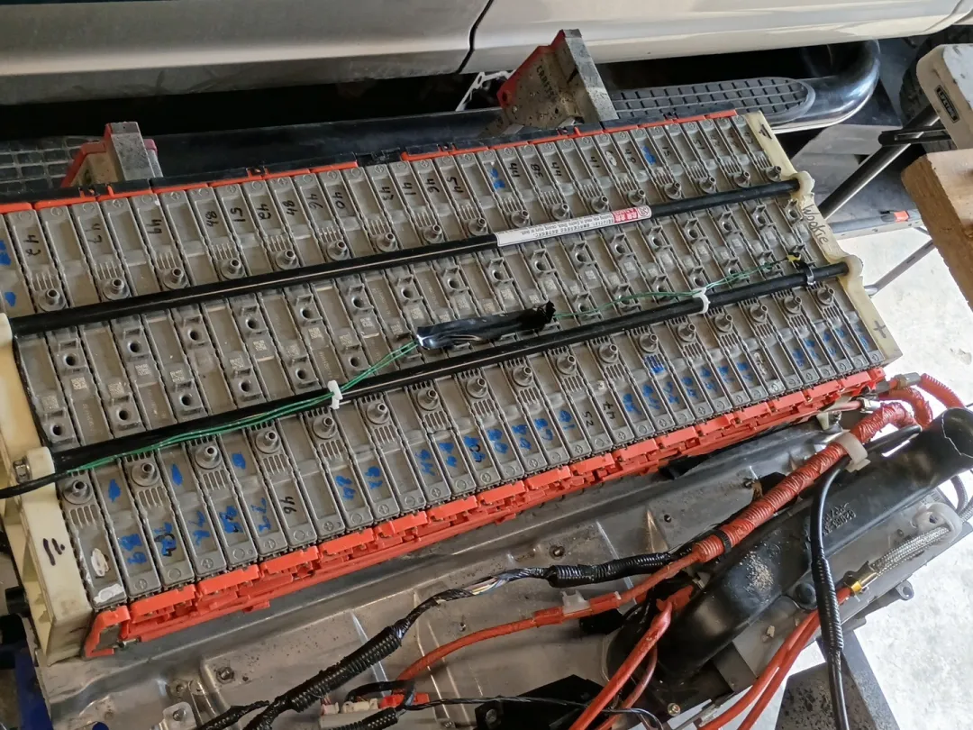 A hybrid battery pack opened on the bench, its rows of modules and orange high voltage cables exposed.