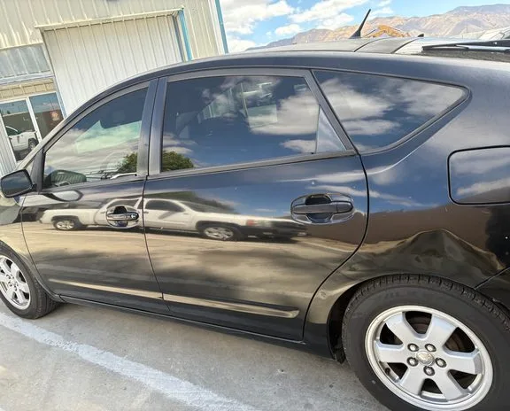 A black Prius parked outside a repair shop.